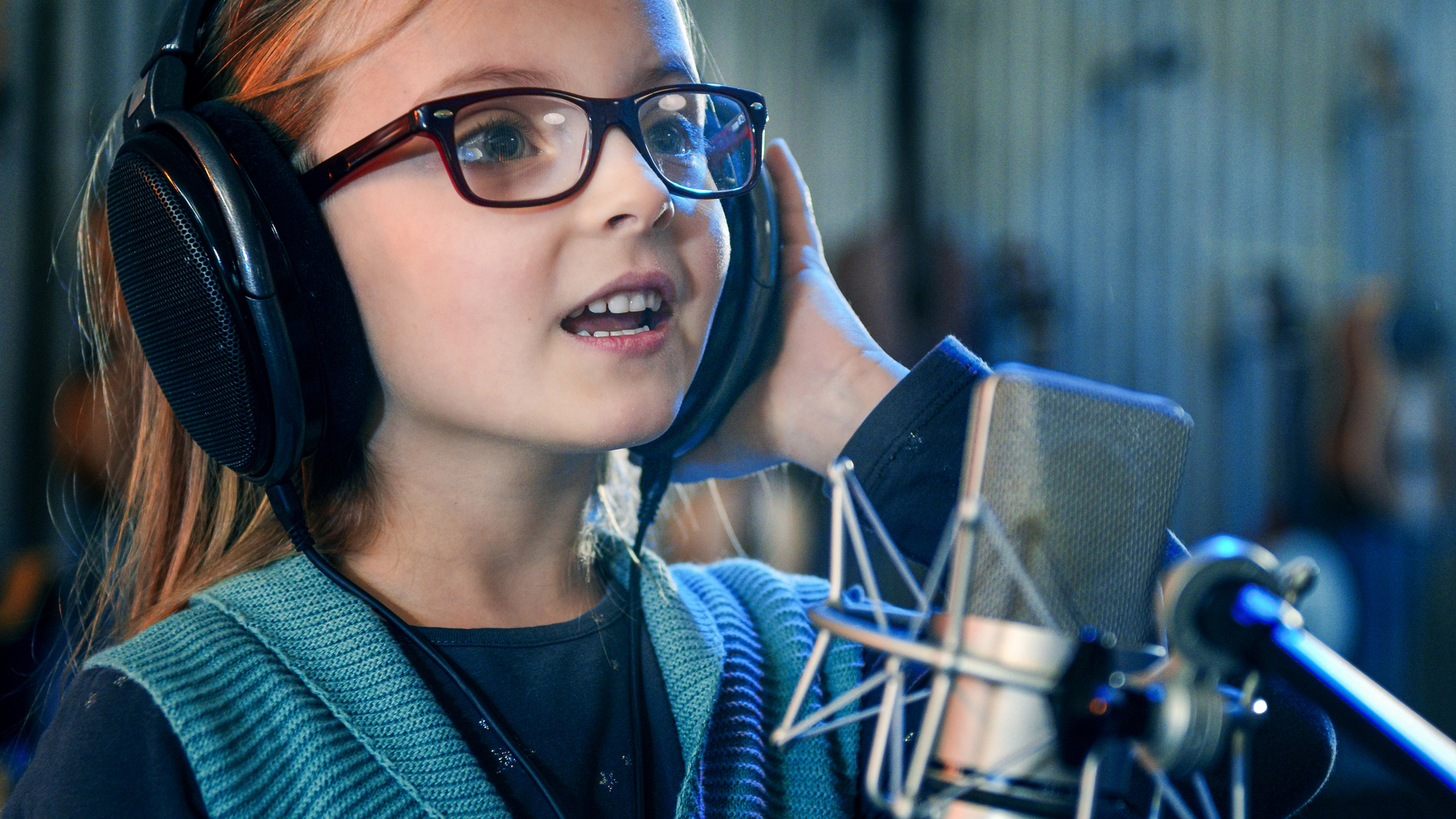 Kid singing in studio.Little girl singing a song.Front view close up. Kid wearing headphones attending singing class.